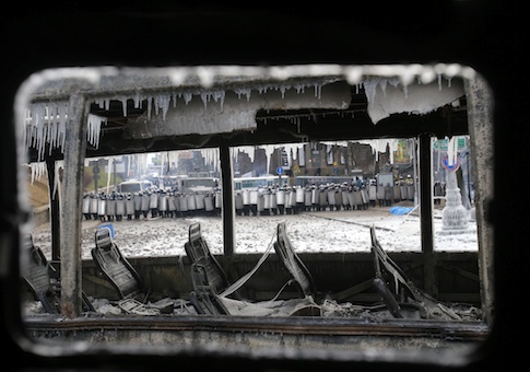Seen through a vehicle torched by protesters overnight, police officers block a street during unrest