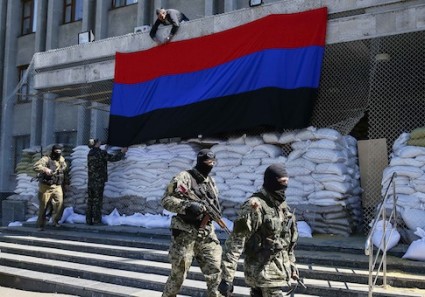 Pro-Russian armed men walk past activists hanging up a "Donetsk Republic" flag outside the mayor's office in Slaviansk