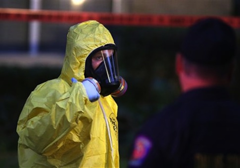 A hazmat worker looks up while finishing up cleaning outside an apartment building of a hospital worker in Dallas, Texas