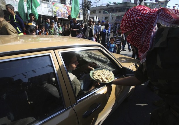 A masked Palestinian distributes sweets as he celebrates with others an attack on a Jerusalem synagogue, in Rafah in the southern Gaza Strip