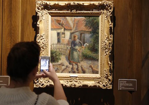 A visitor takes a photograph of a painting called 'Shepherdess Bringing in Sheep' that the Nazis stole / AP