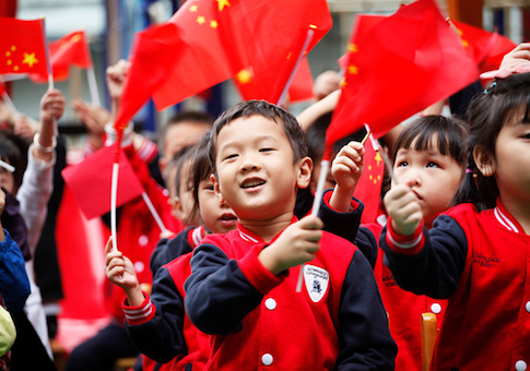 Children wave national flags as they sing revolutionary songs to celebrate the upcoming National Day at a kindergarten